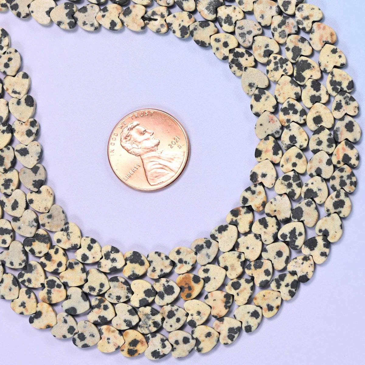 Matte dalmatian jasper flat heart beads in chalky oatmeal cream scattered with charcoal black spots.