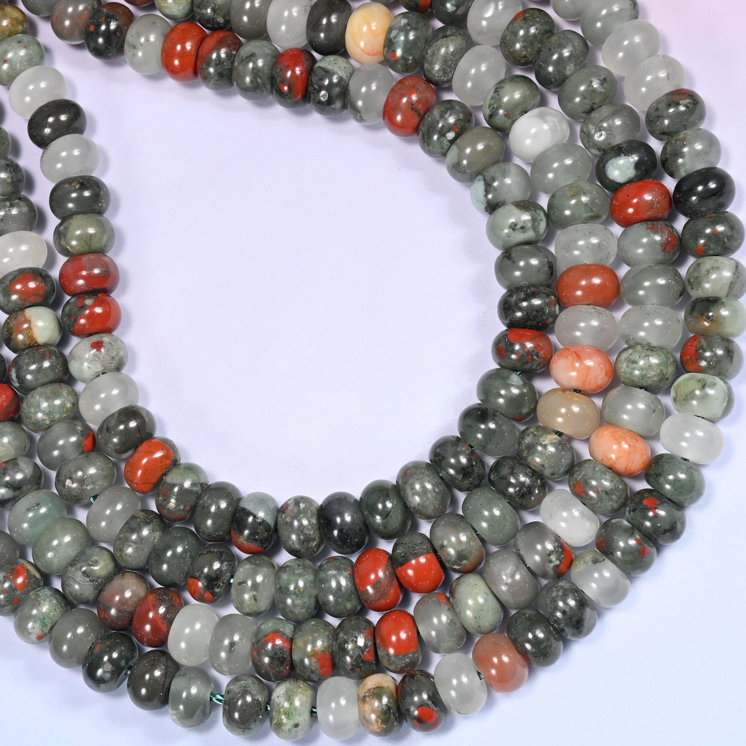Circular coil of African Bloodstone bead strands on a lavender background with a penny in the center for size comparison.