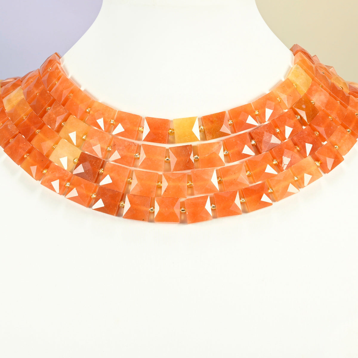 Natural red aventurine faceted flat square strands arranged as a layered collar on a white display bust, orange-red beads across the neck