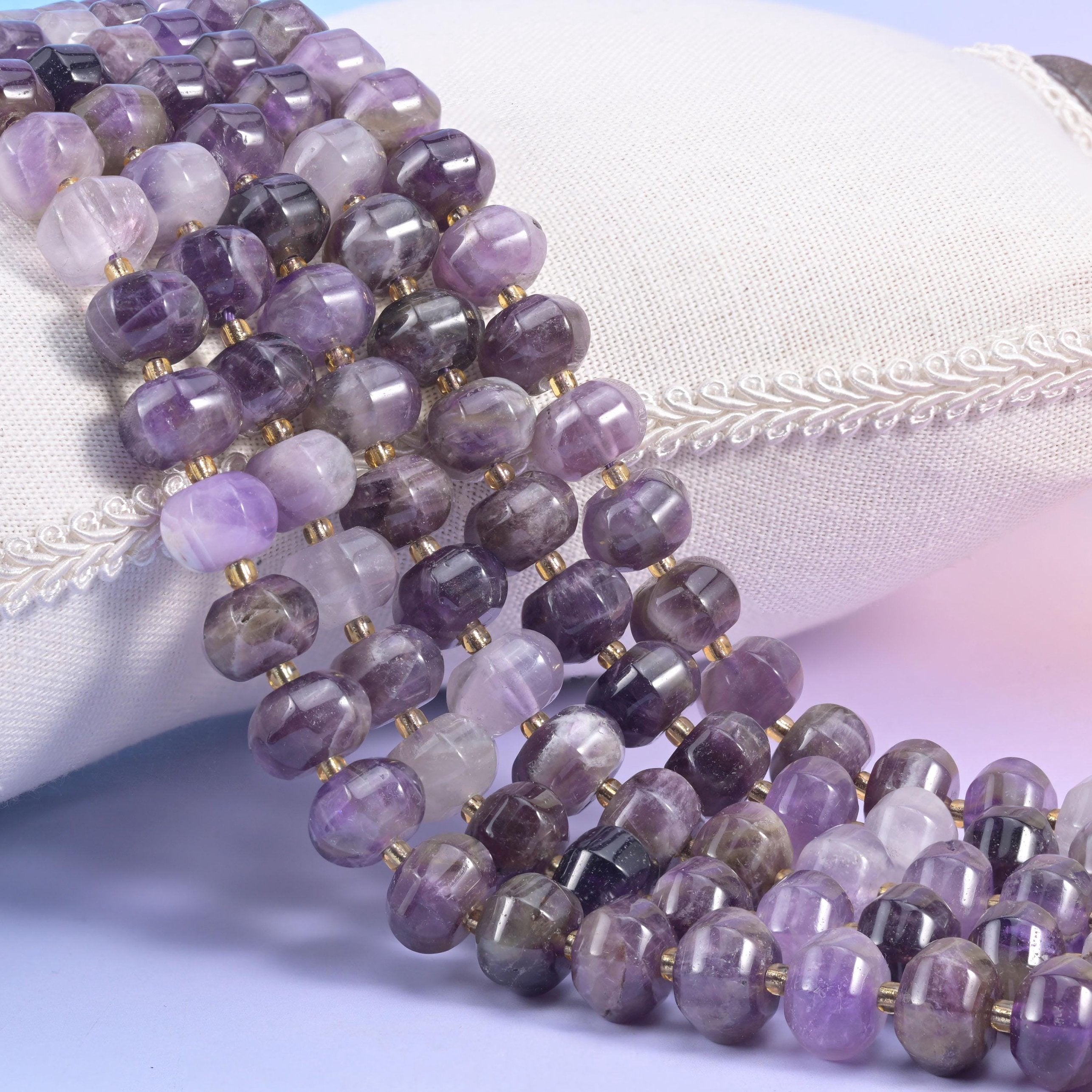 Banded Amethyst pumpkin rondelles tumbling off a cream cushion, purple and white striping visible across the beads