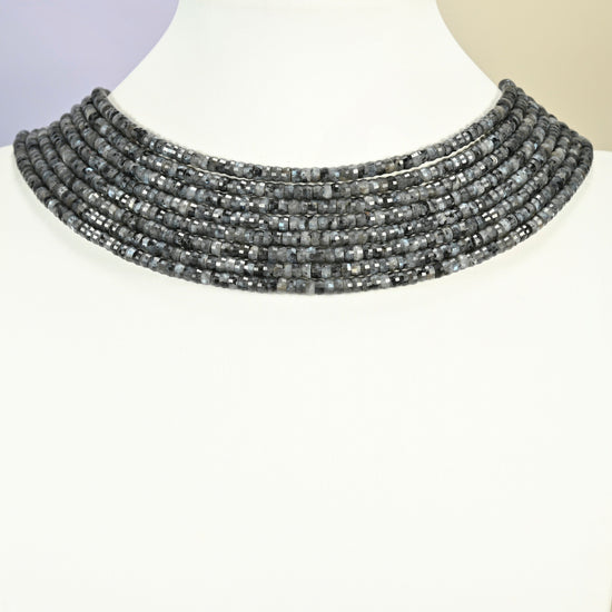 Black labradorite faceted heishi disc strands arranged as a layered collar on a white display bust, dark gray beads across the neck