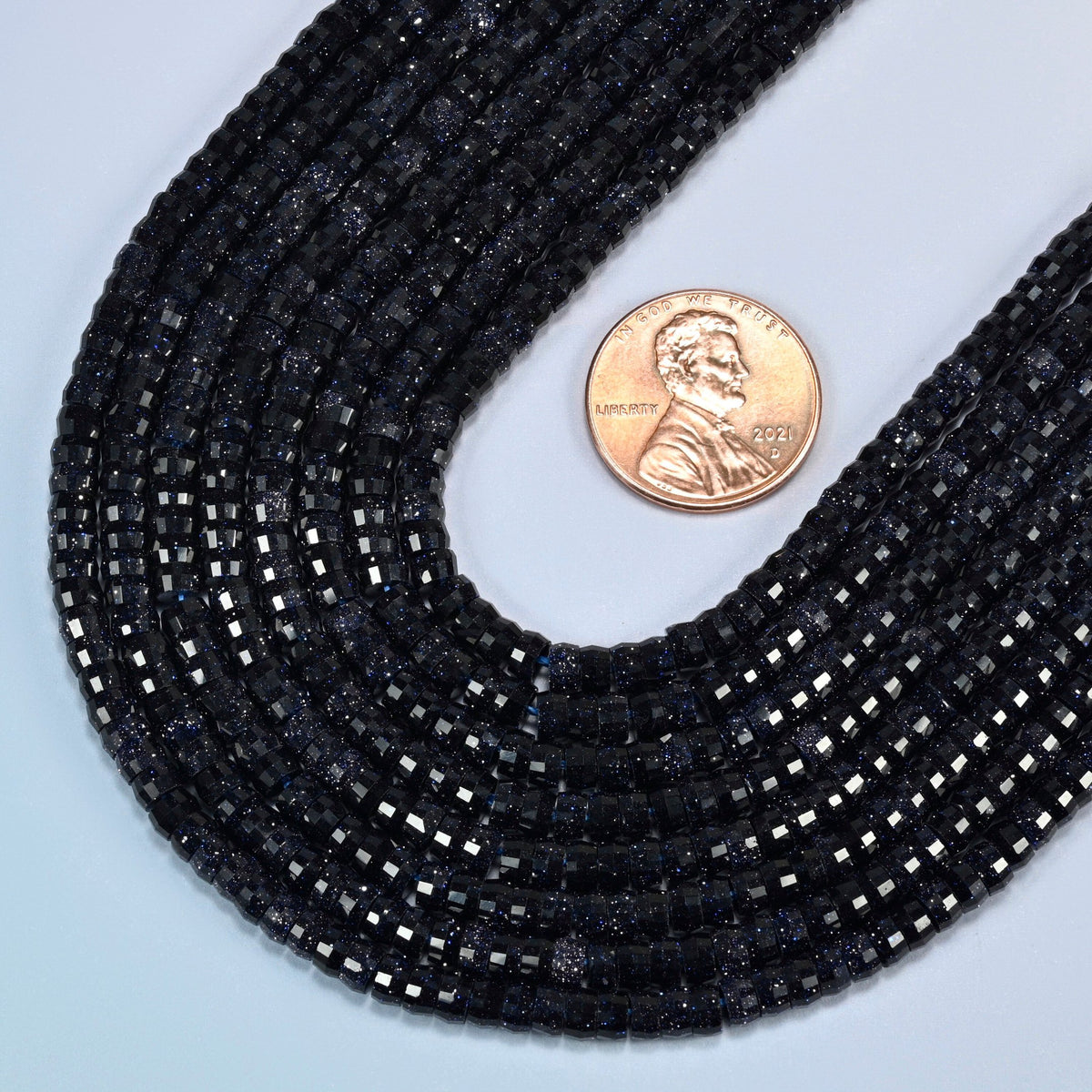 Close view of blue sandstone faceted heishi disc strands curving beside a US penny for scale