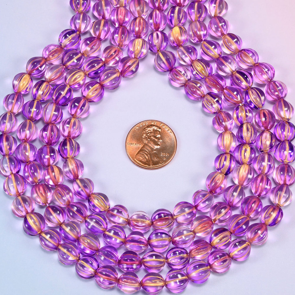 Purple gold pumpkin glass beads coiled into a ring, shown with a US penny in the open center for scale.