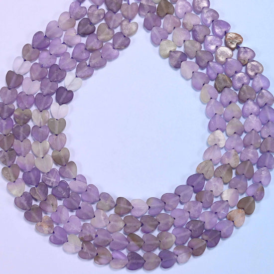 Multiple strands of purple and lavender amethyst flat heart-shaped beads laid side by side for color comparison