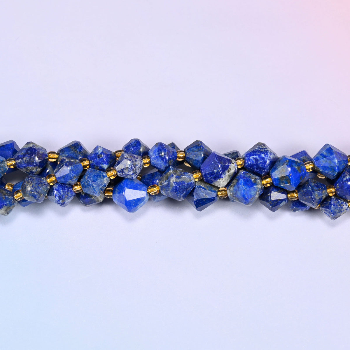 Lapis lazuli bicone beads shown as a single strand laid straight across, a few beads almost solid blue, others heavily veined.