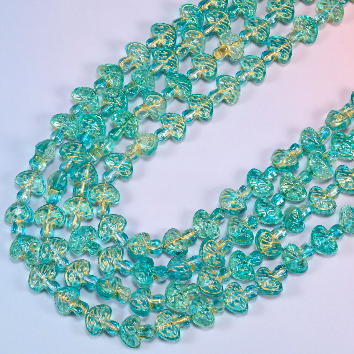 Aqua gold flat mushroom glass beads laid in a wide shallow bend, transparent aqua glass with a light gold wash picking out the gill lines.