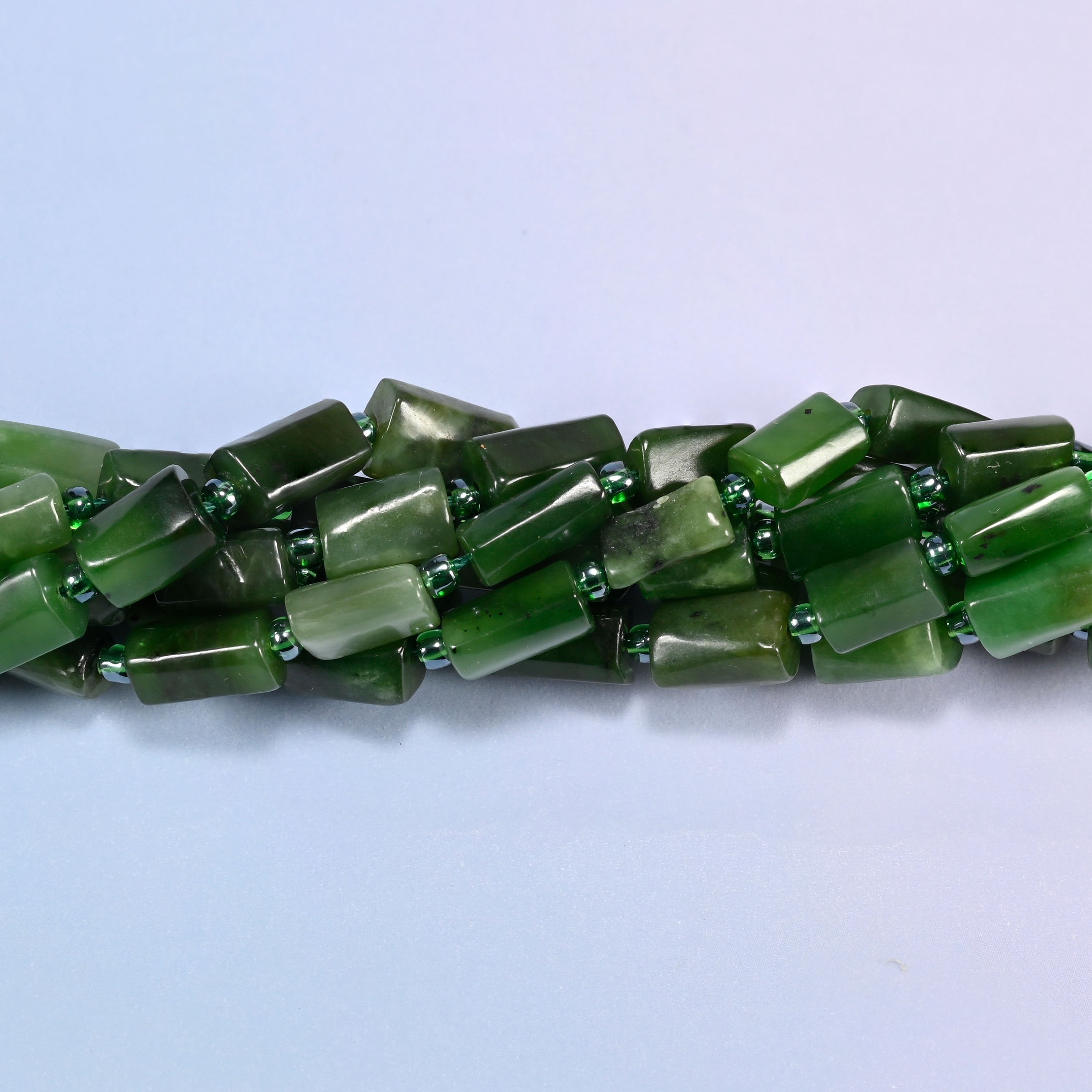 Close-up of Canadian Green Jade faceted tube beads showing the flat cut planes, glossy polish and green glass seed bead spacers