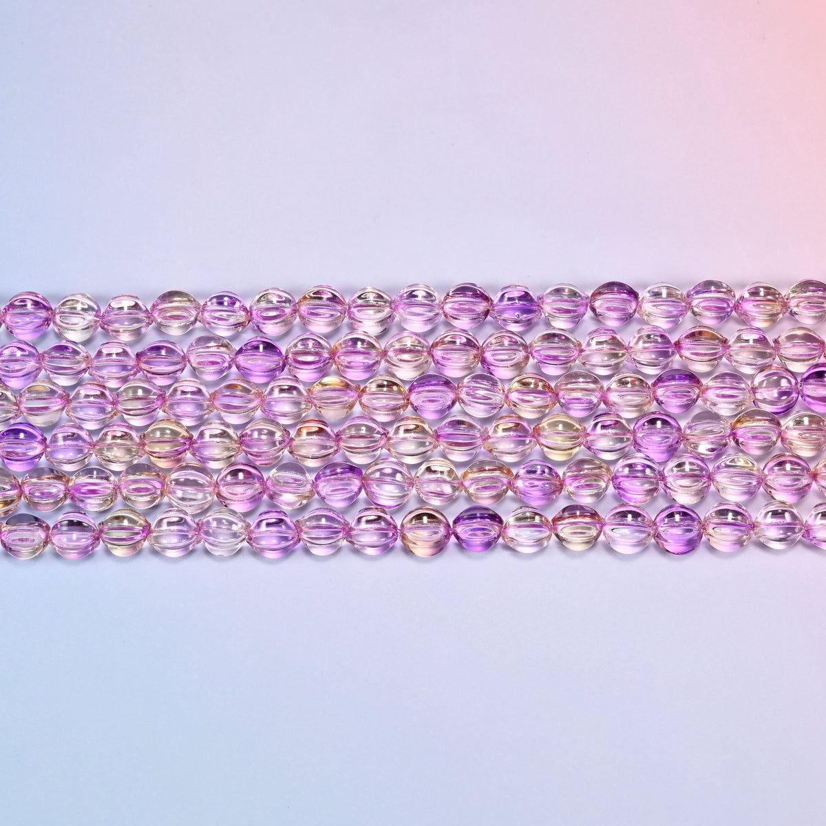 Close-up of 8mm clear purple gold pumpkin glass beads in four horizontal rows, showing the carved melon ribs.