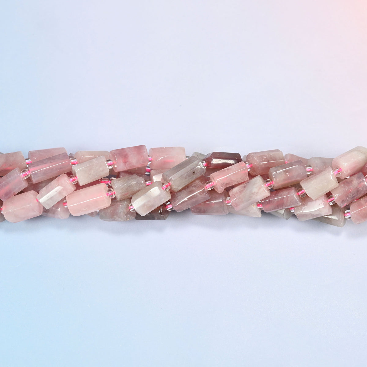 Madagascar multi color rose quartz faceted tube beads crossing the frame in a shallow wave of overlapping strands.