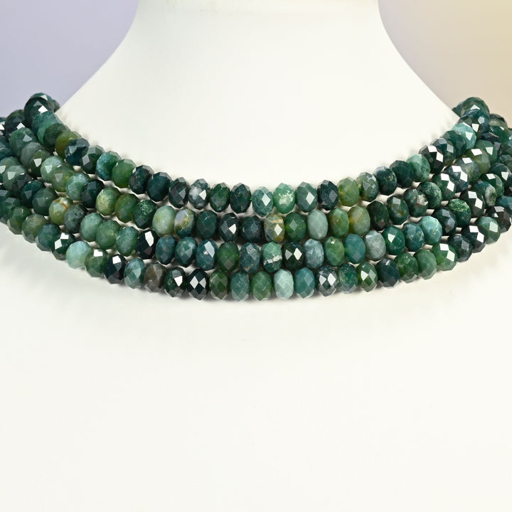 Moss agate faceted rondelle beads laid in collar rows across a white display bust.