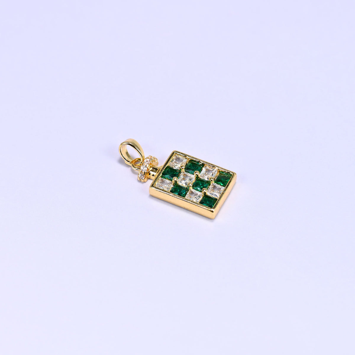 Single green perfume bottle zirconia charm angled on lavender, its raised gold bezel and square cut green and clear stones catching the light.