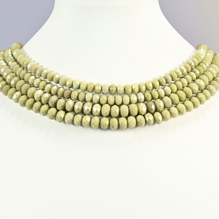 Green alashan agate beads shown on a white neck display, four faceted rondelle strands layered close to the neckline