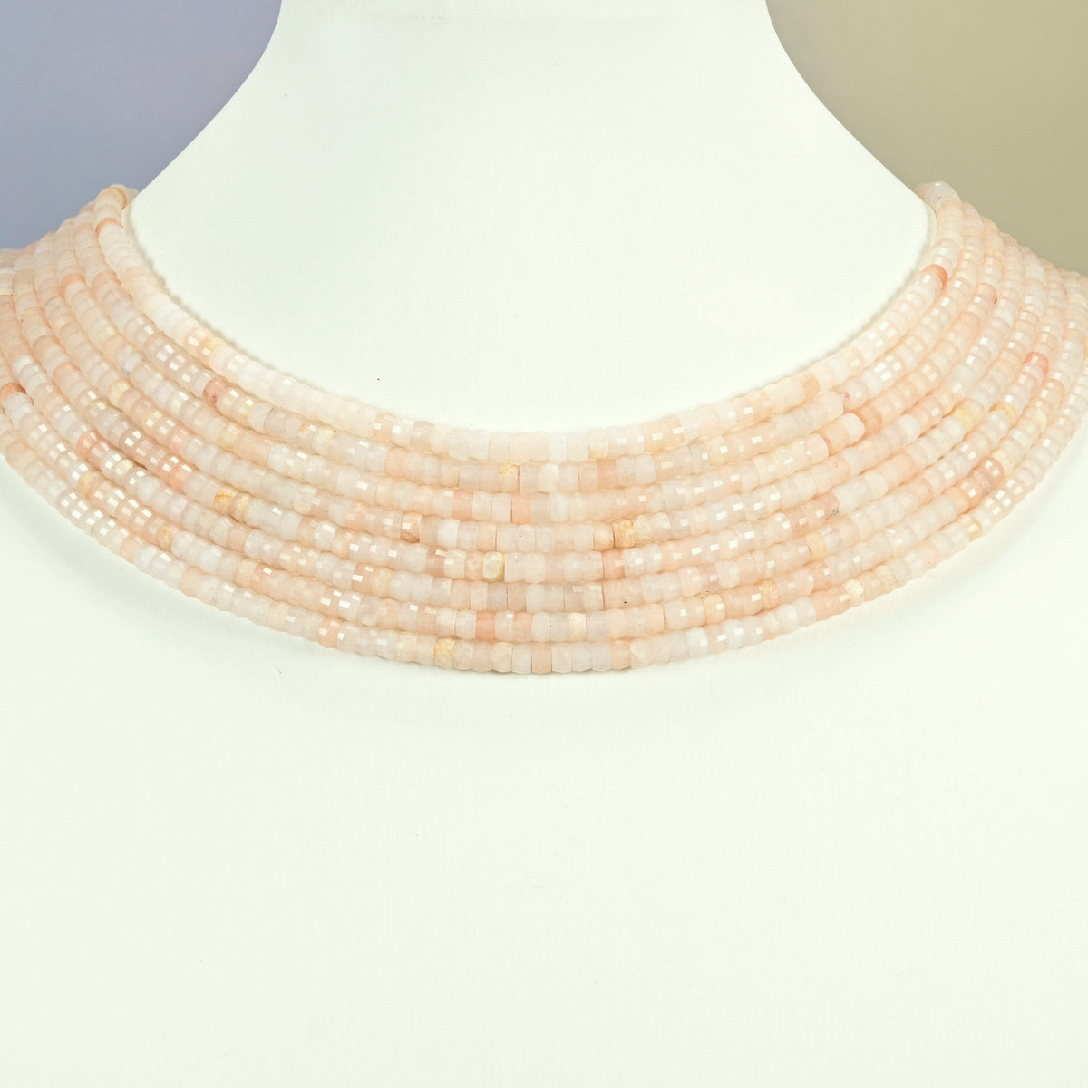 Pink aventurine faceted heishi disc strands arranged as a layered collar on a white display bust, light pink beads across the neck