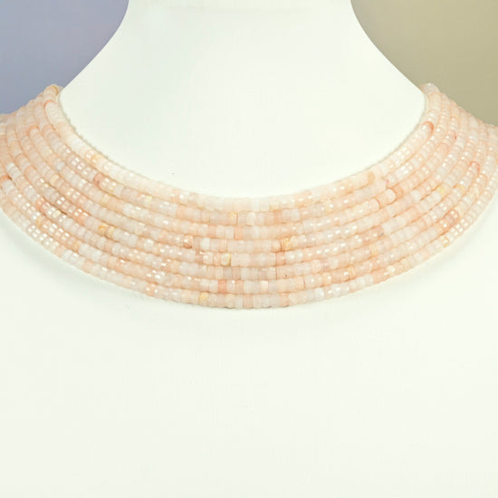 Pink aventurine faceted heishi disc strands arranged as a layered collar on a white display bust, light pink beads across the neck