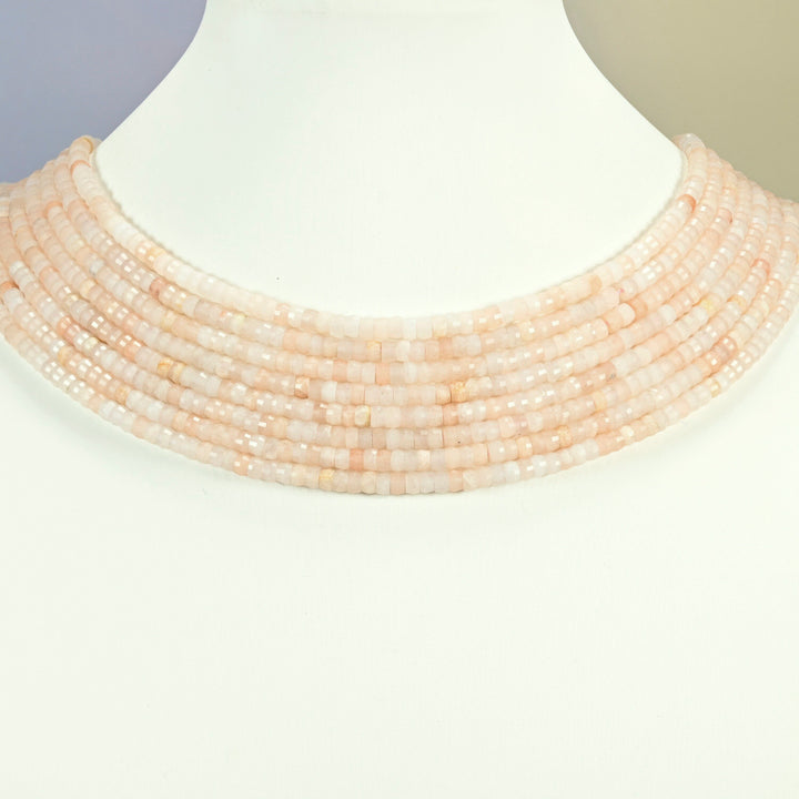 Pink aventurine faceted heishi disc strands arranged as a layered collar on a white display bust, light pink beads across the neck