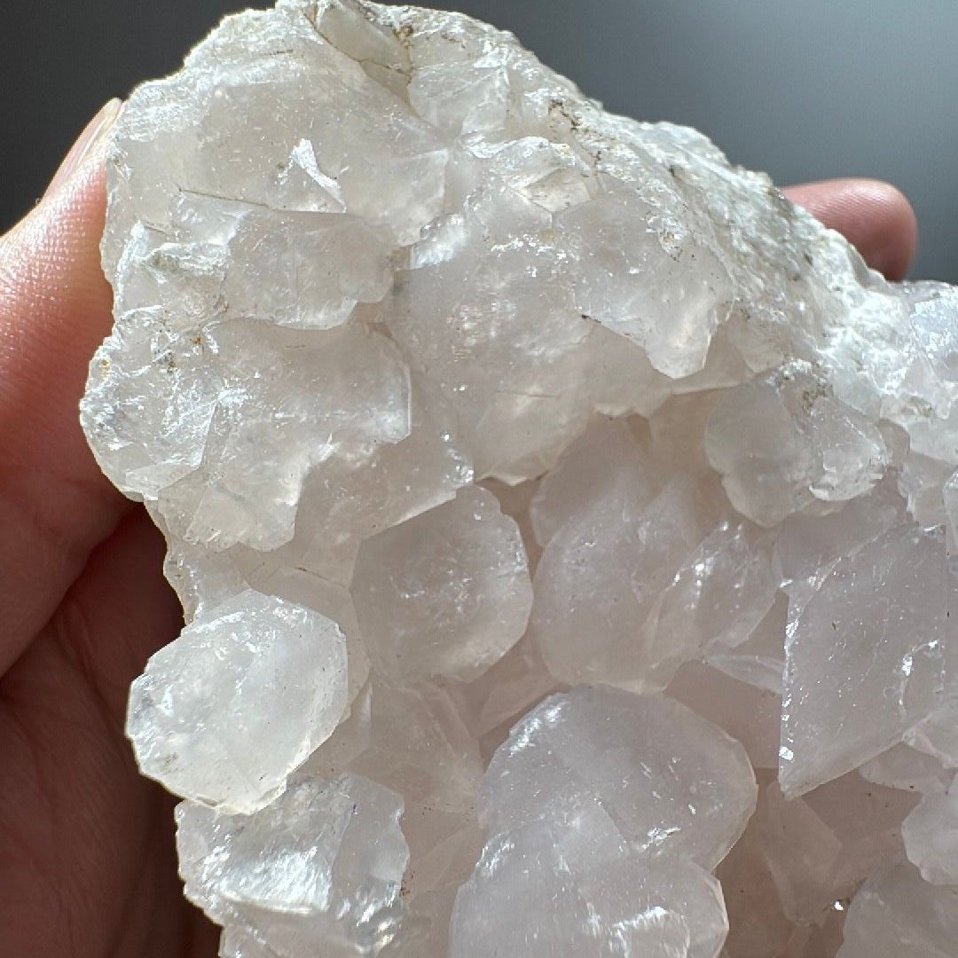 Angled view of the calcite cluster catching window light along the crystal edges