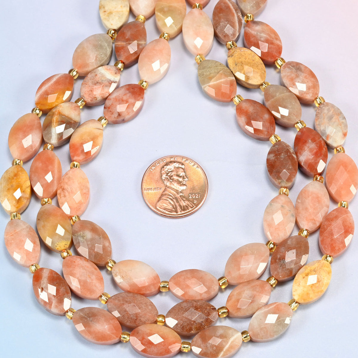 Red crazy agate faceted flat oval strands formed into a teardrop loop around a US penny for scale
