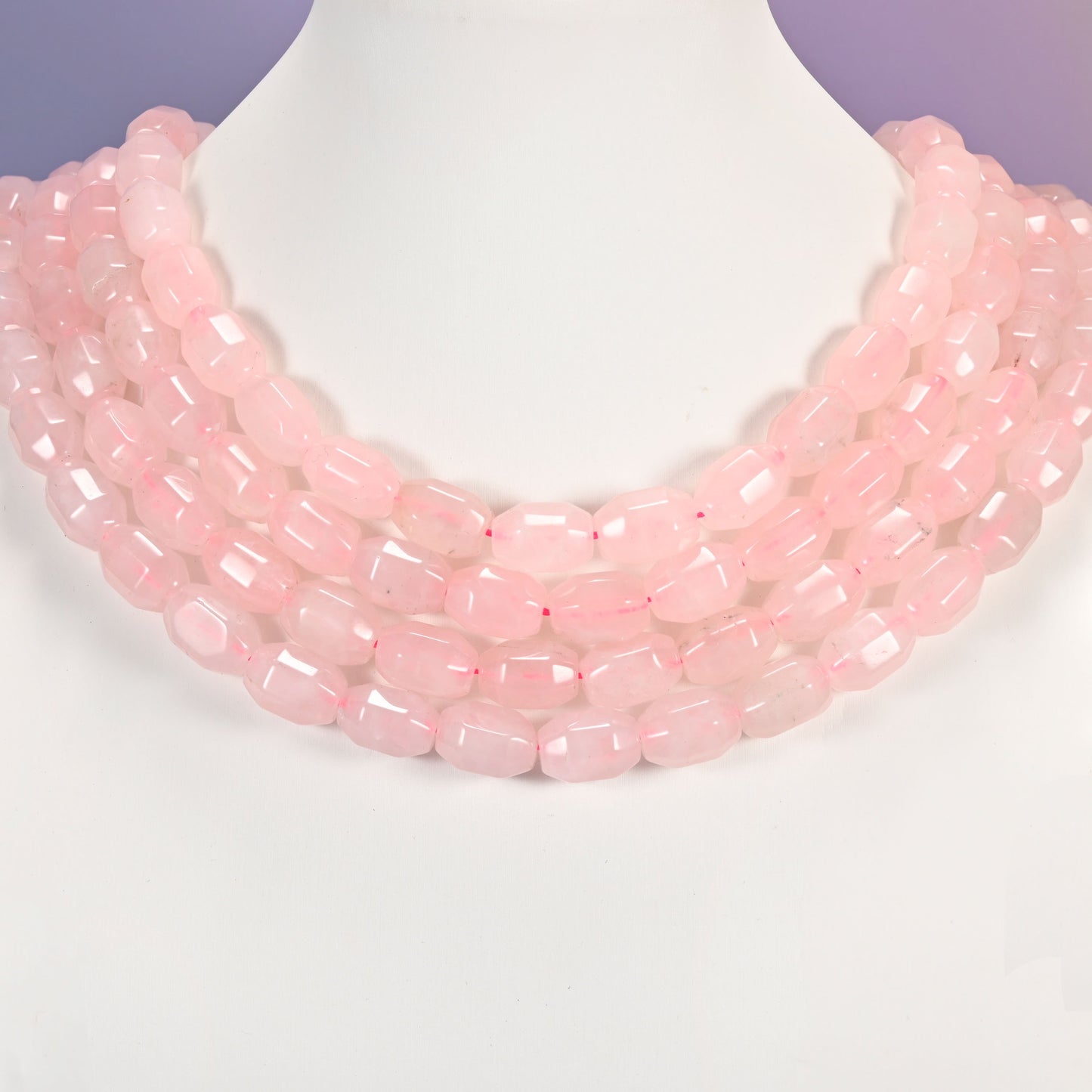 Multi-strand necklace of Rose Quartz faceted barrel beads laid on a white mannequin neck form against a lavender background.