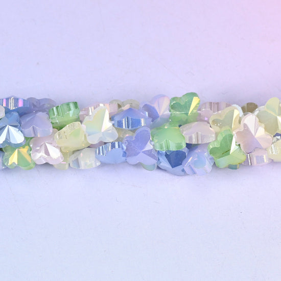 Small pressed-glass butterflies in a pastel mix of periwinkle blue, mint green, lemon, lilac and cream, each with a satin-frosted surface and a soft pearly sheen across the open wings.