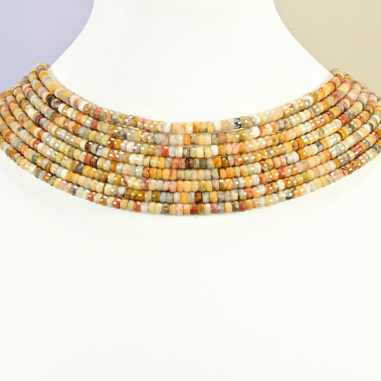Crazy agate faceted heishi disc strands arranged as a layered collar on a white display bust, yellow and tan beads across the neck