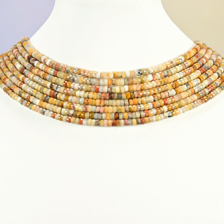 Crazy agate faceted heishi disc strands arranged as a layered collar on a white display bust, yellow and tan beads across the neck