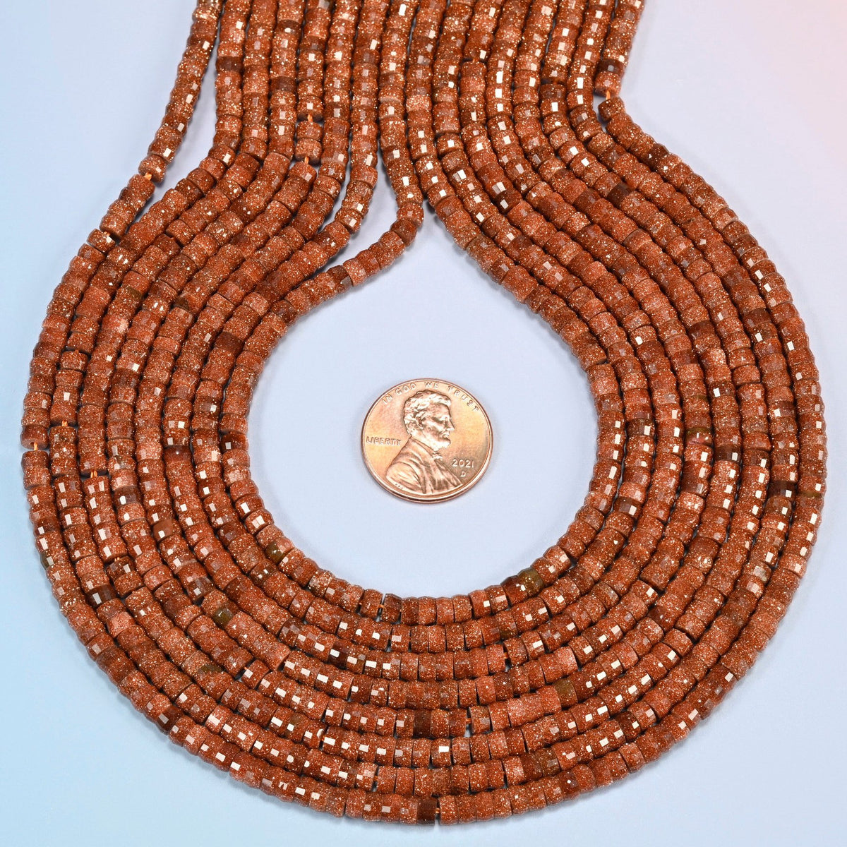 Gold sandstone faceted heishi disc strands formed into a teardrop loop around a US penny for scale
