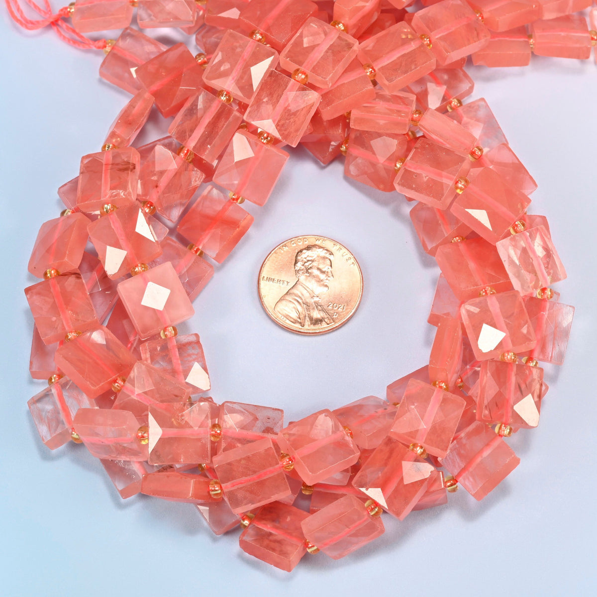 Melon quartz faceted flat square beads 10x10mm coiled in a loop around a US penny for scale, close-up of the faceted flat square shape