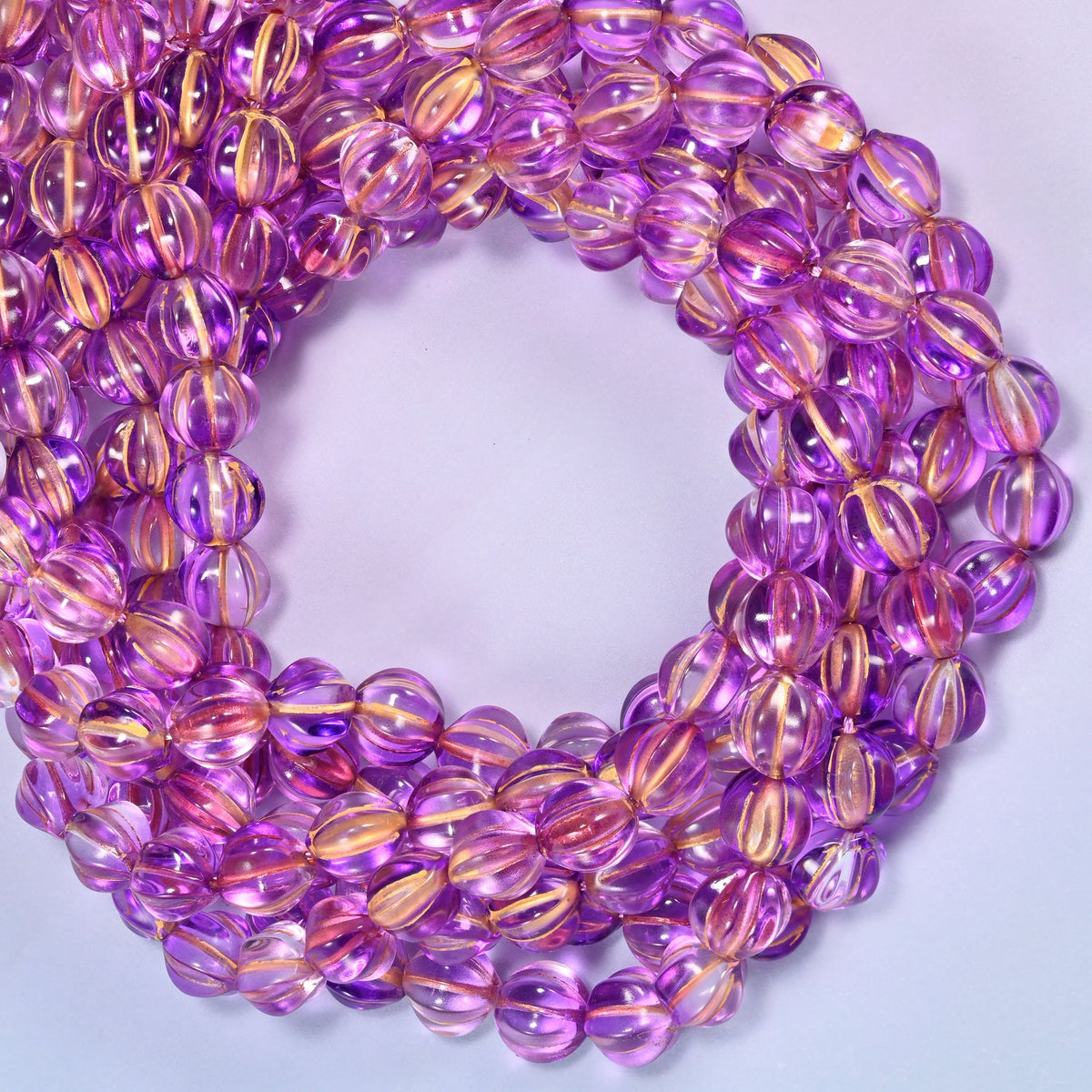 Purple gold pumpkin glass beads coiled with the open center to one side, showing the fluted grooves end on.