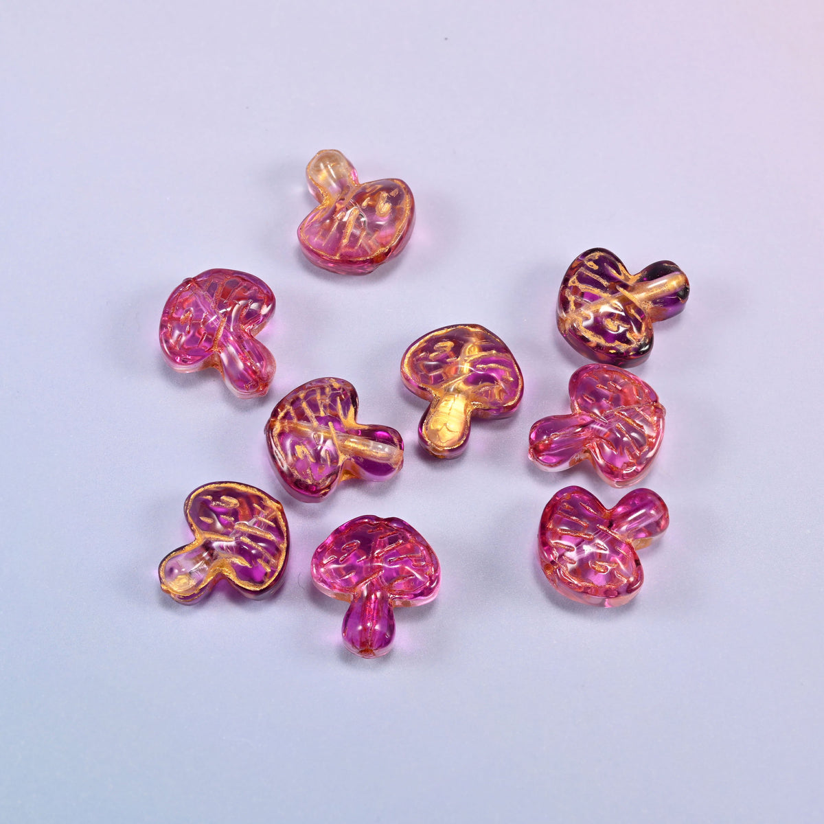 A scattered group of loose 13x12mm pink gold flat mushroom glass beads, showing the gill lines under each cap.