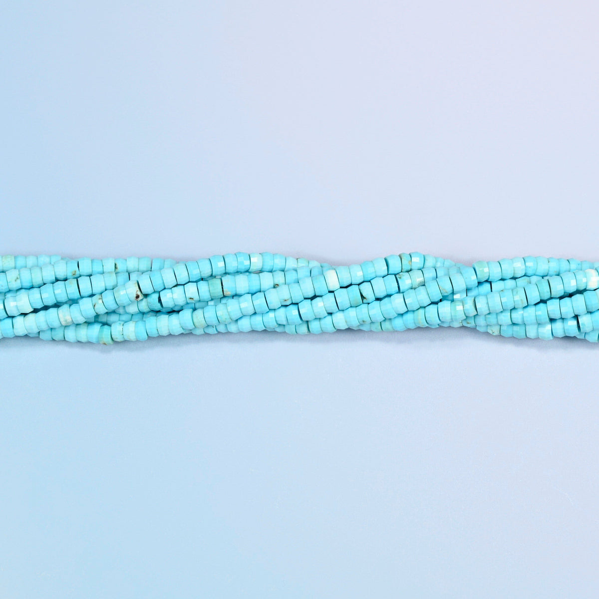 Strands of dyed blue howlite faceted heishi disc beads twisted together in a horizontal row