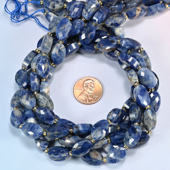 Orange sodalite faceted flat oval beads 9x14mm coiled in a loop around a US penny for scale, close-up of the faceted flat oval shape