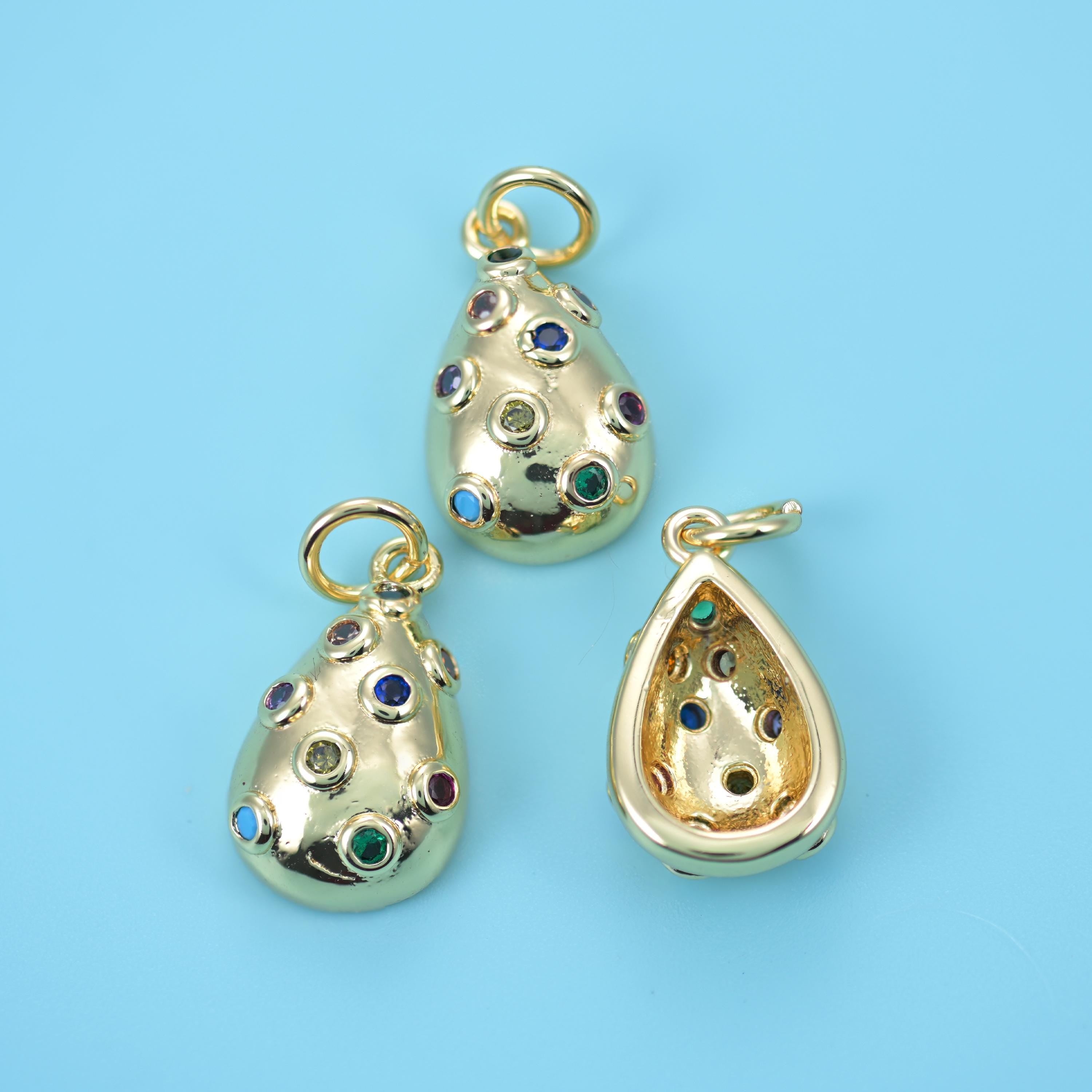 A plump domed teardrop in warm polished gold, scattered with small flush-set zircons in blue, red, green and clear so the…