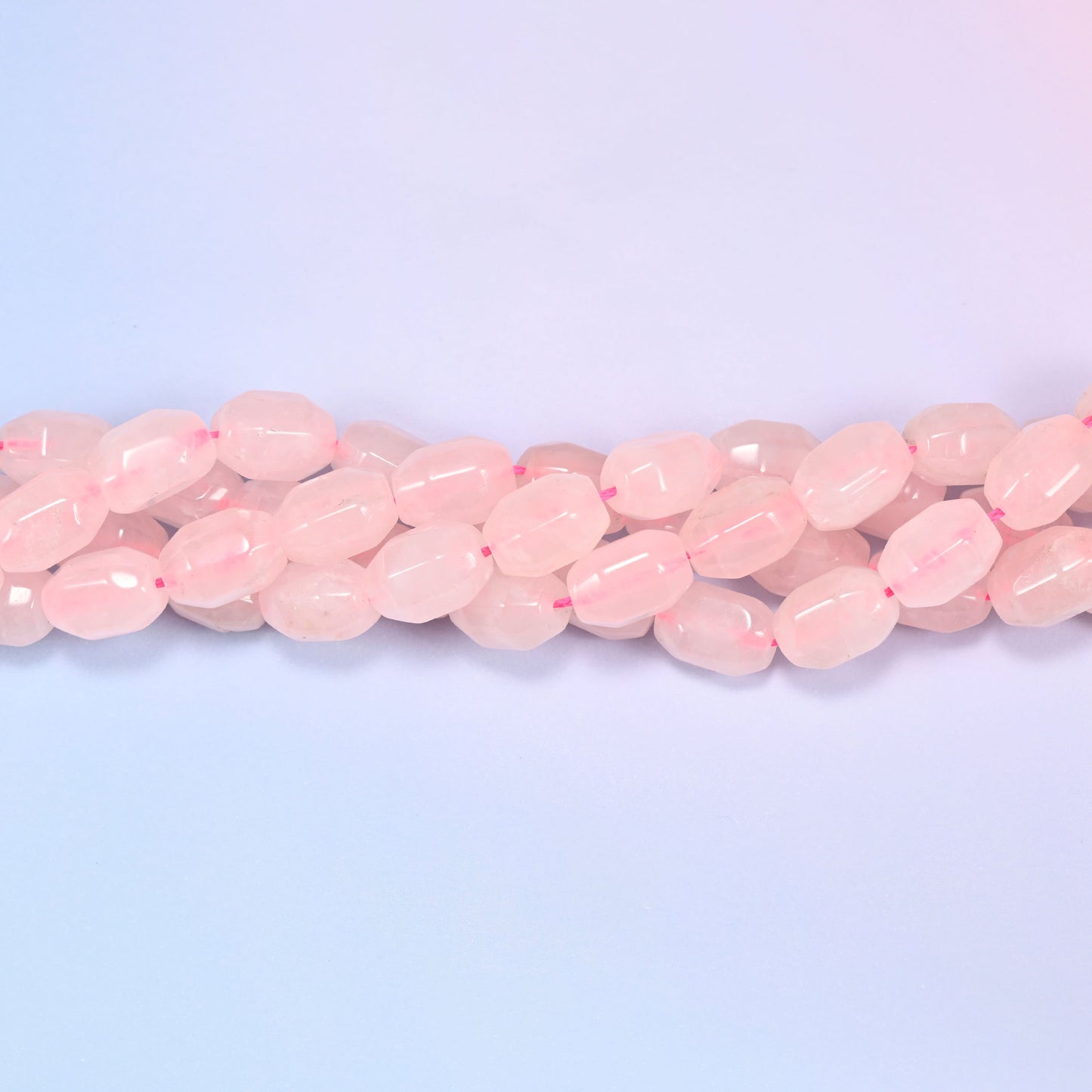 Close-up horizontal row of Rose Quartz faceted barrel beads laid straight, showing the polished facet detail and pink stringing thread.
