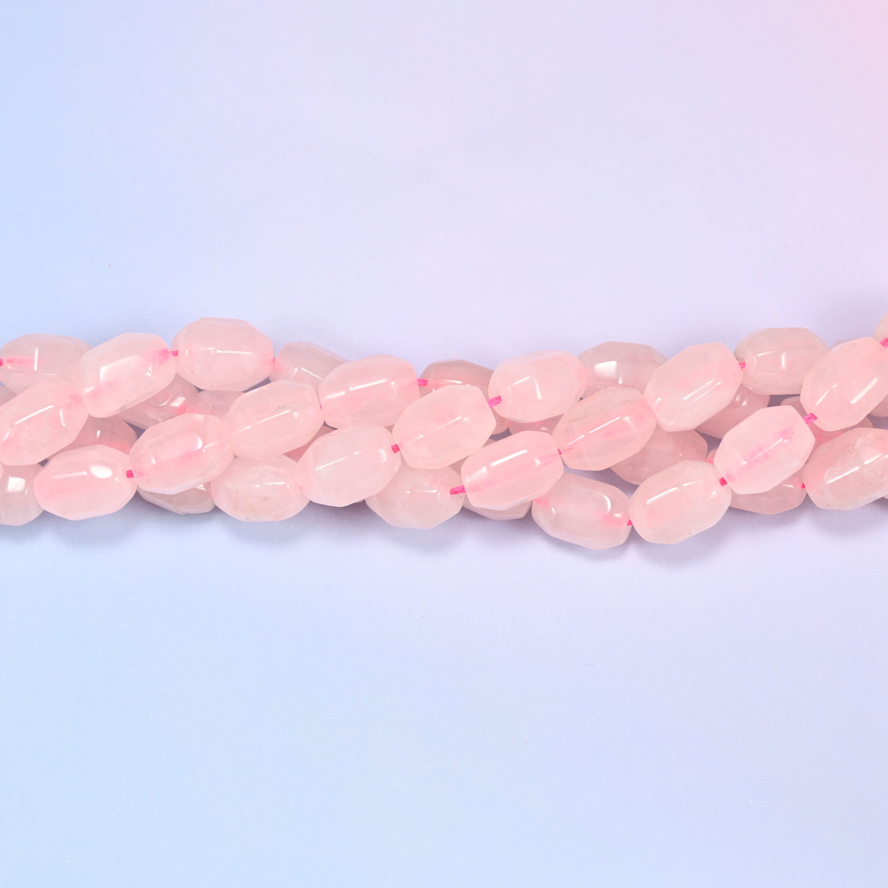 Close-up horizontal row of Rose Quartz faceted barrel beads laid straight, showing the polished facet detail and pink stringing thread.