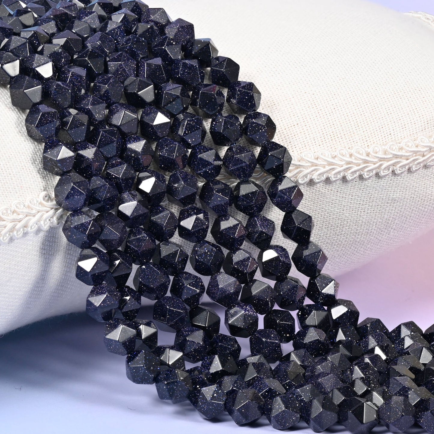 Strands of deep midnight blue Blue Sandstone star cut beads resting over a white display pillow