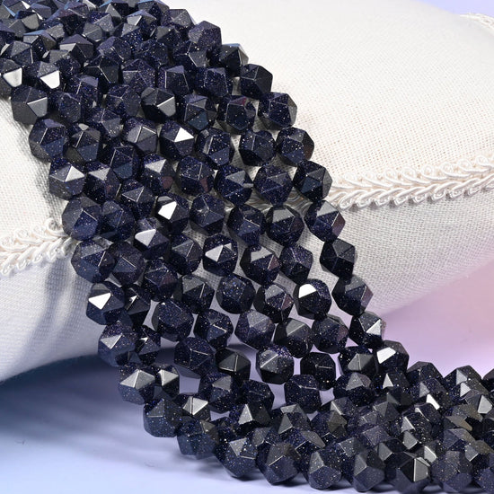 Strands of deep midnight blue Blue Sandstone star cut beads resting over a white display pillow