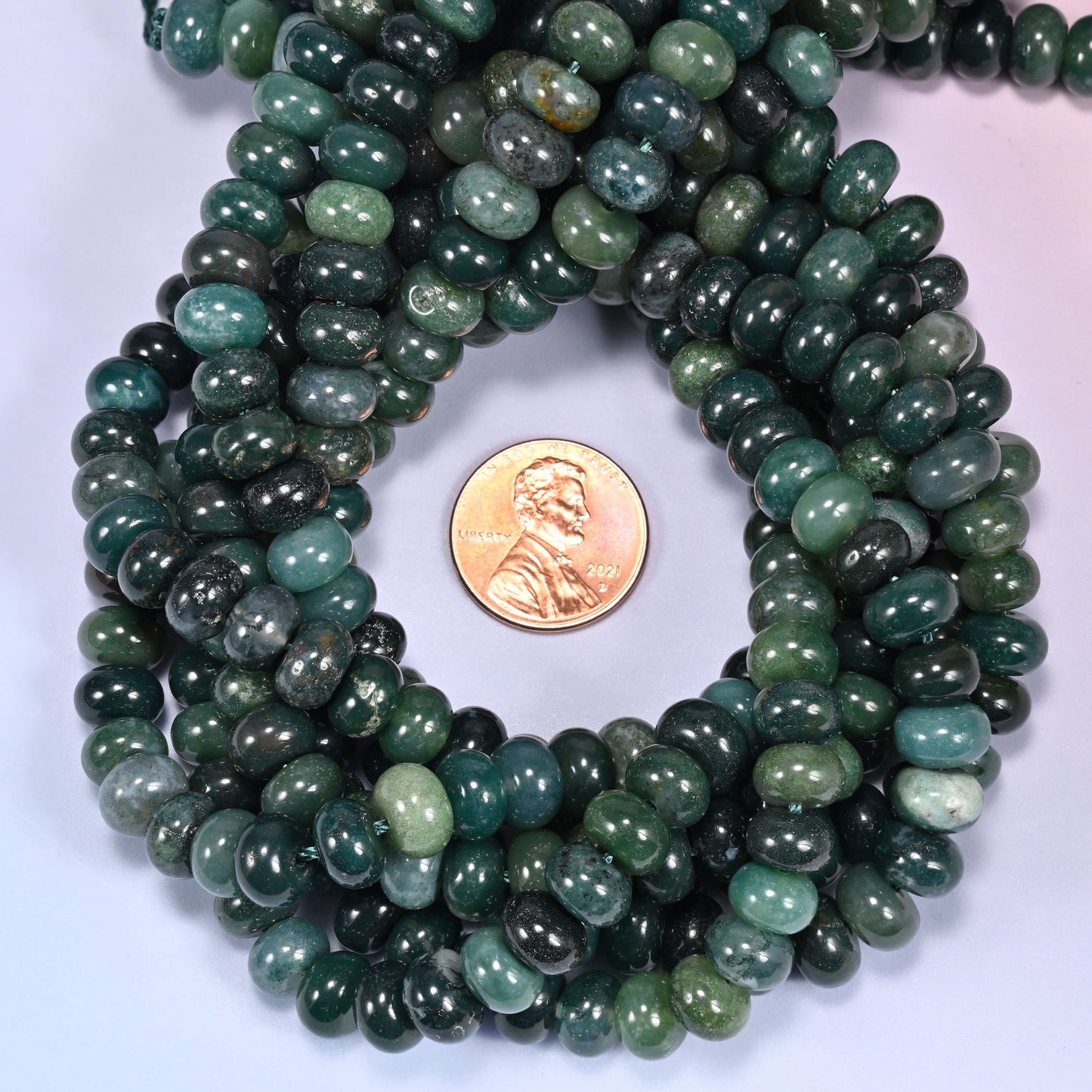 Multiple strands of Moss Agate beads gathered together on a lavender surface, loose ends visible.