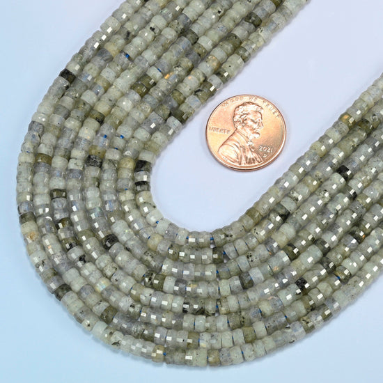 Close view of white labradorite faceted heishi disc strands curving beside a US penny for scale