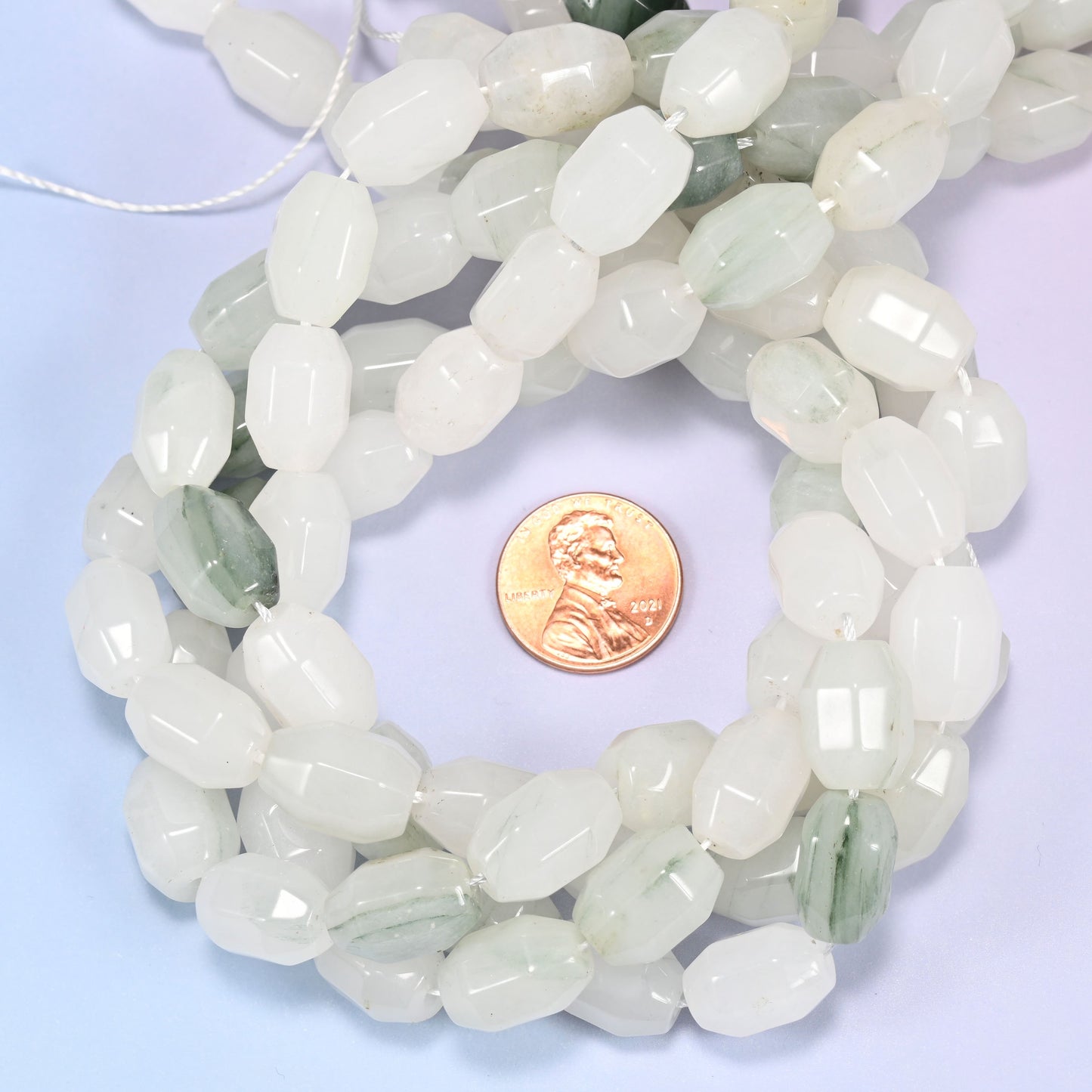 Close-up circular coil of Tianshan Jade faceted barrel bead strands with a penny in the center for size comparison.