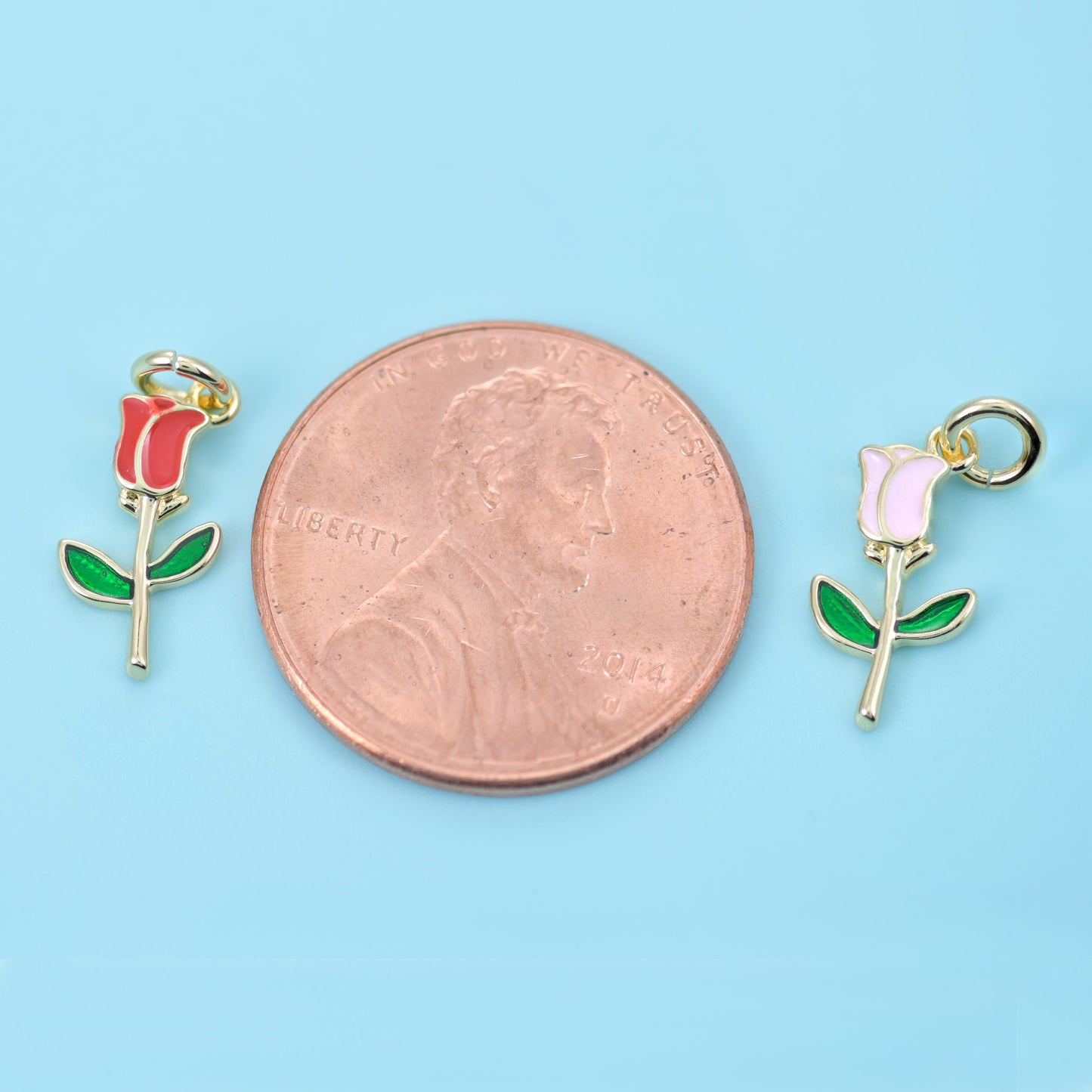 A single long-stemmed rosebud just over a centimetre tall, with a red or soft pink enamel bloom, green enamel leaves and a…