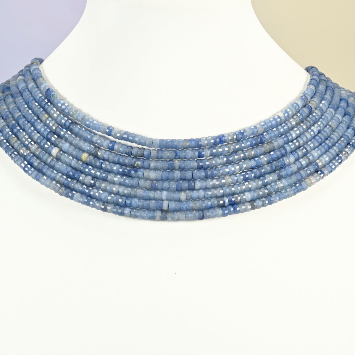 Blue aventurine faceted heishi disc strands arranged as a layered collar on a white display bust, light blue beads across the neck