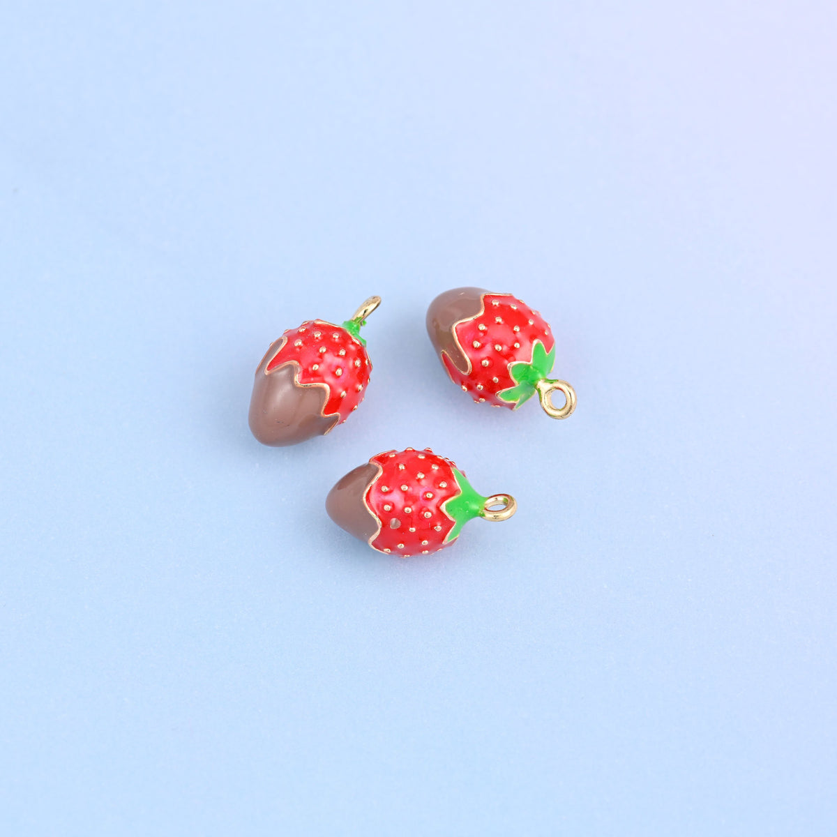 Three strawberry charms dipped in brown enamel, red berry above with white seed dots and a green leaf top.