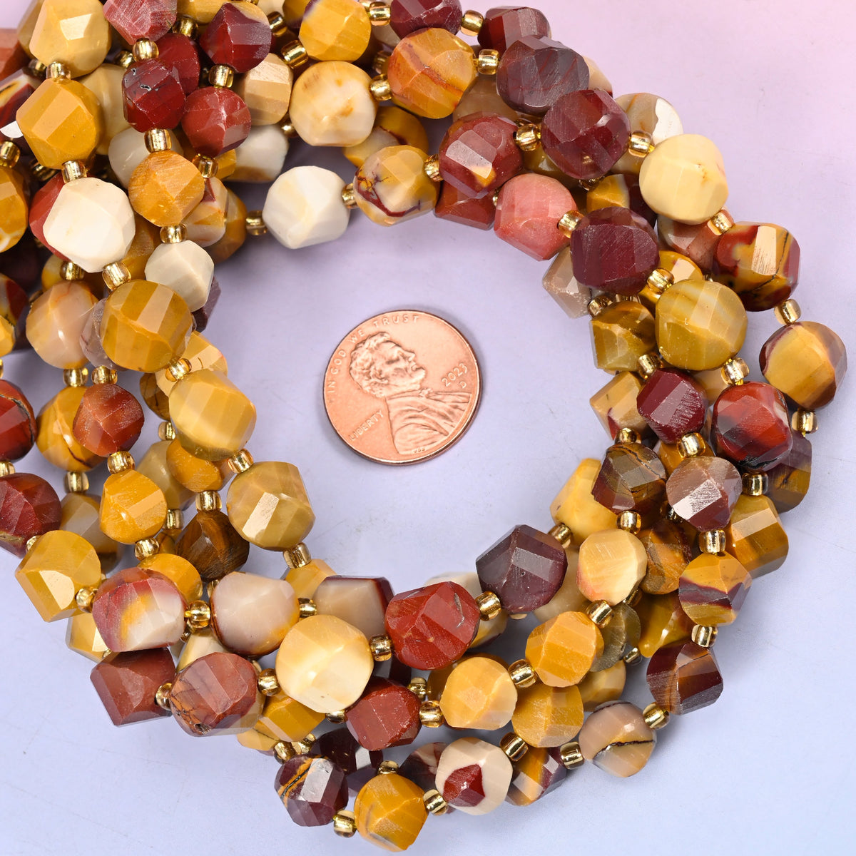 Mookaite faceted spiral twist bead strands coiled around a US penny for size reference