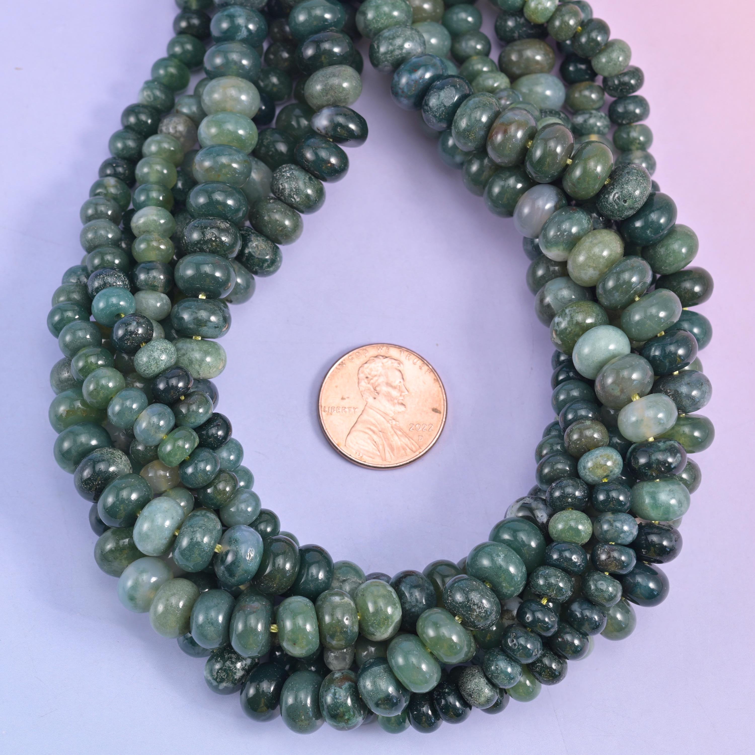 Moss agate smooth rondelle beads draped around a US penny for size reference.