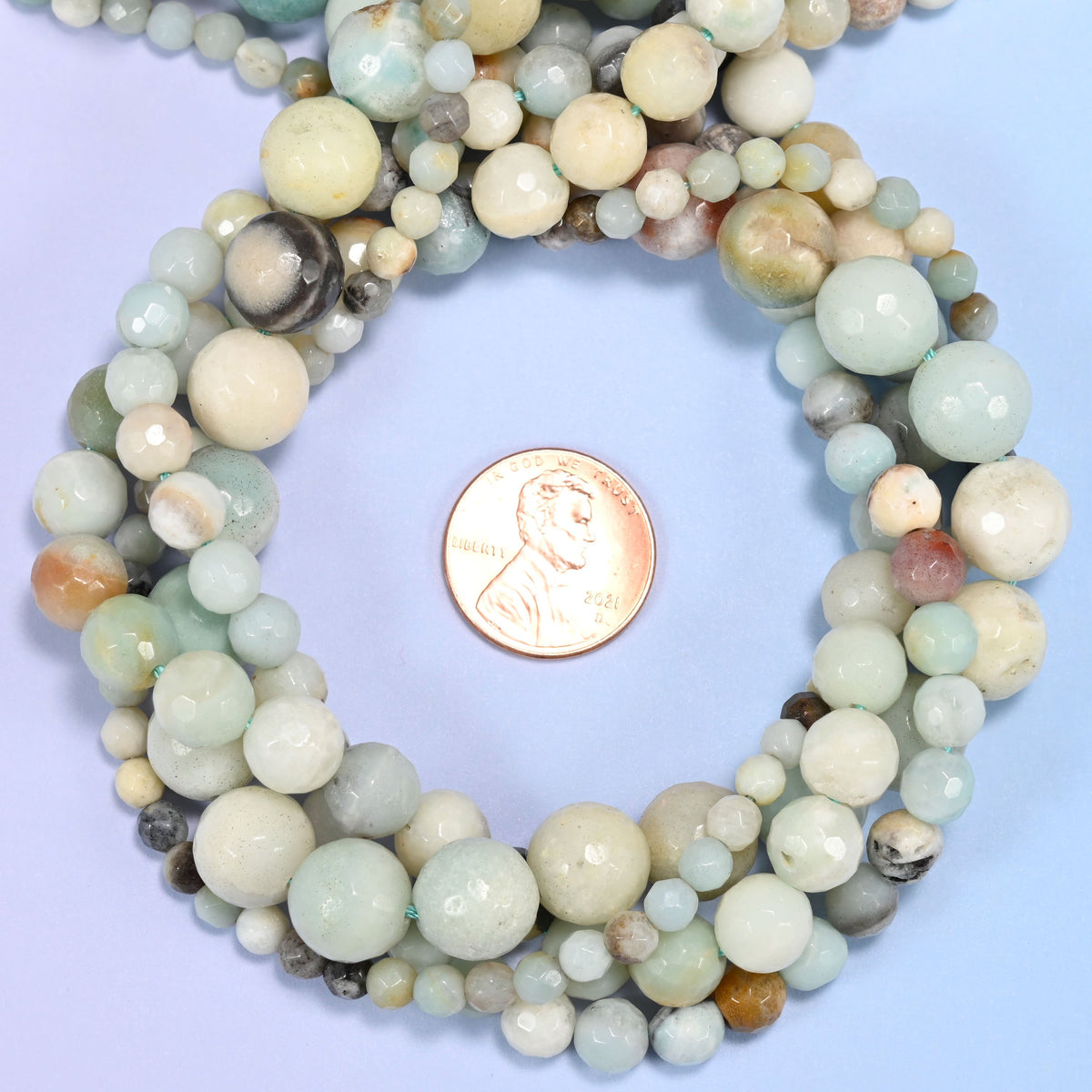 Multicolor Amazonite faceted round bead strands coiled around a US penny for size reference