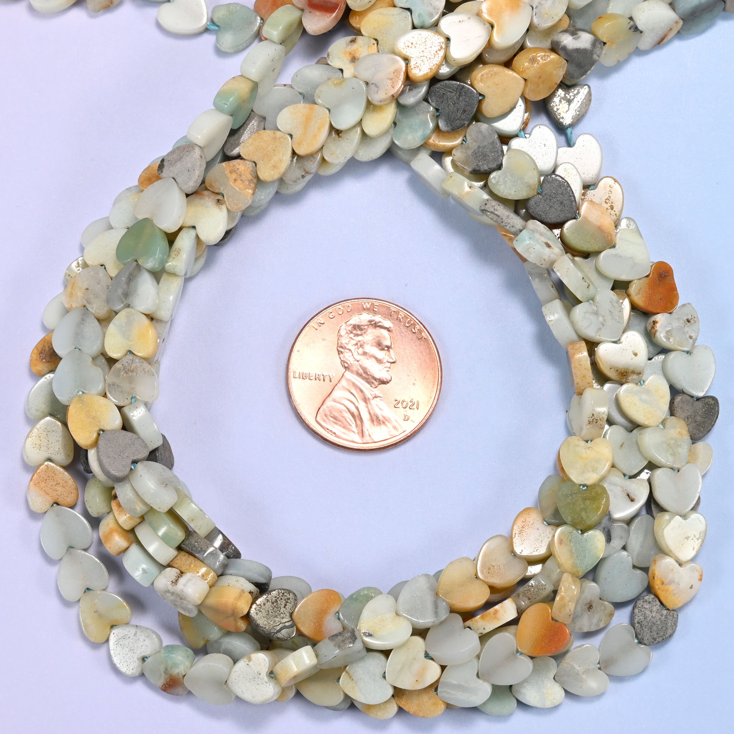 Multicolor Amazonite flat heart bead strands coiled around a US penny for size reference