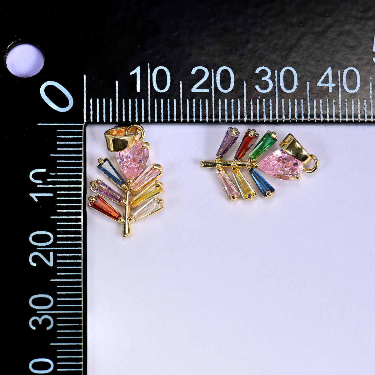 Two multicolour leaf charms shown front and back beside a millimetre ruler for scale