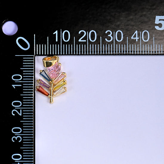 Multicolour leaf charm in gold with a pink stone and green, blue and orange baguette stones, beside a millimetre ruler for scale