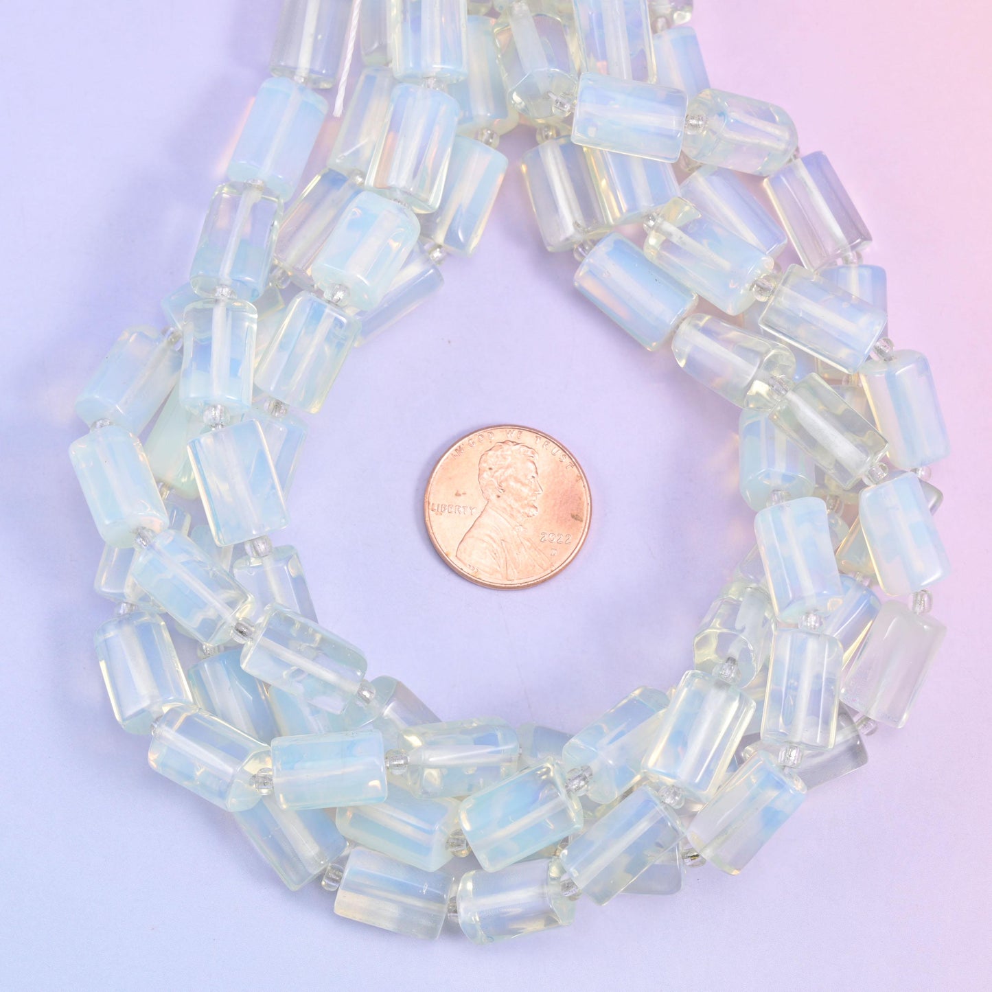 Opalite faceted tube beads coiled around a US penny for size reference, beads about 12x8mm.