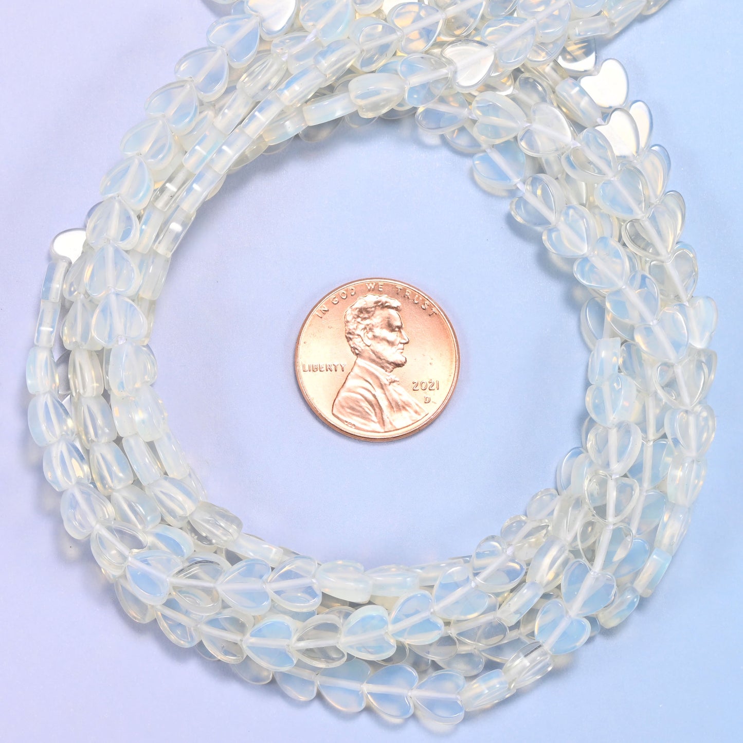 Opalite flat heart bead strands coiled around a US penny for size reference
